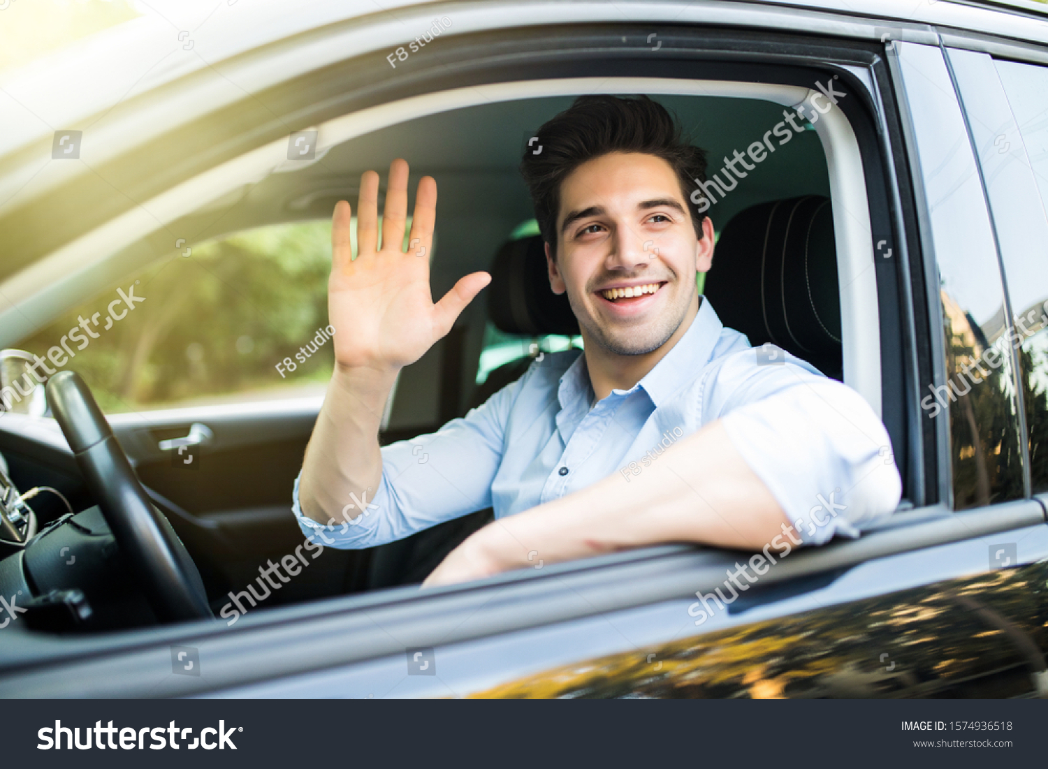 Portrait of young attractive handsome brunette man driving car and greeting somebody with hand. #1574936518