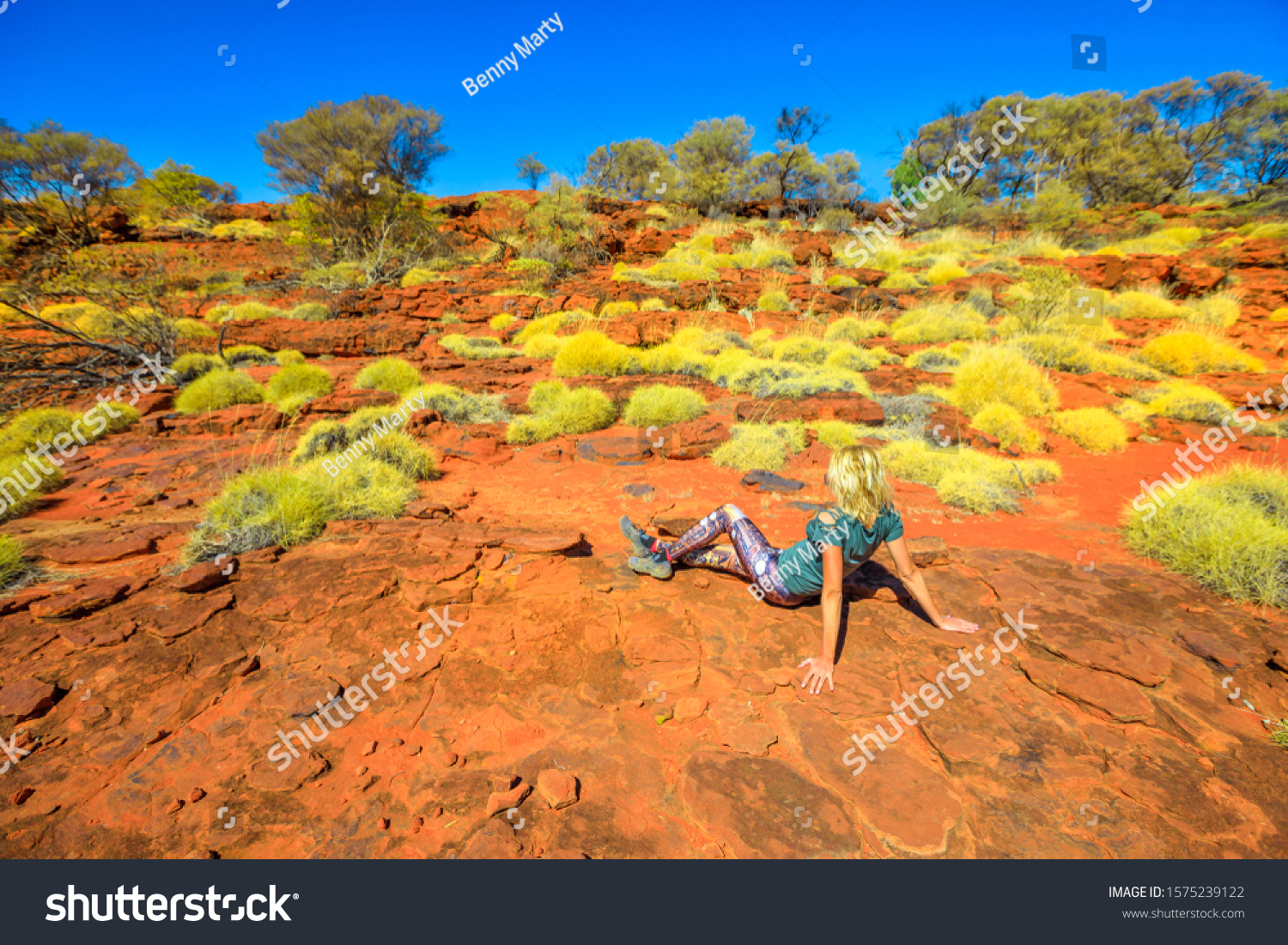 Tourist woman relaxing during the hiking along Arankaia Walk with bush vegetation and red desert sand in Palm Valley, Finke Gorge National Park. Tourism in Australia Outback, Northern Territory. #1575239122
