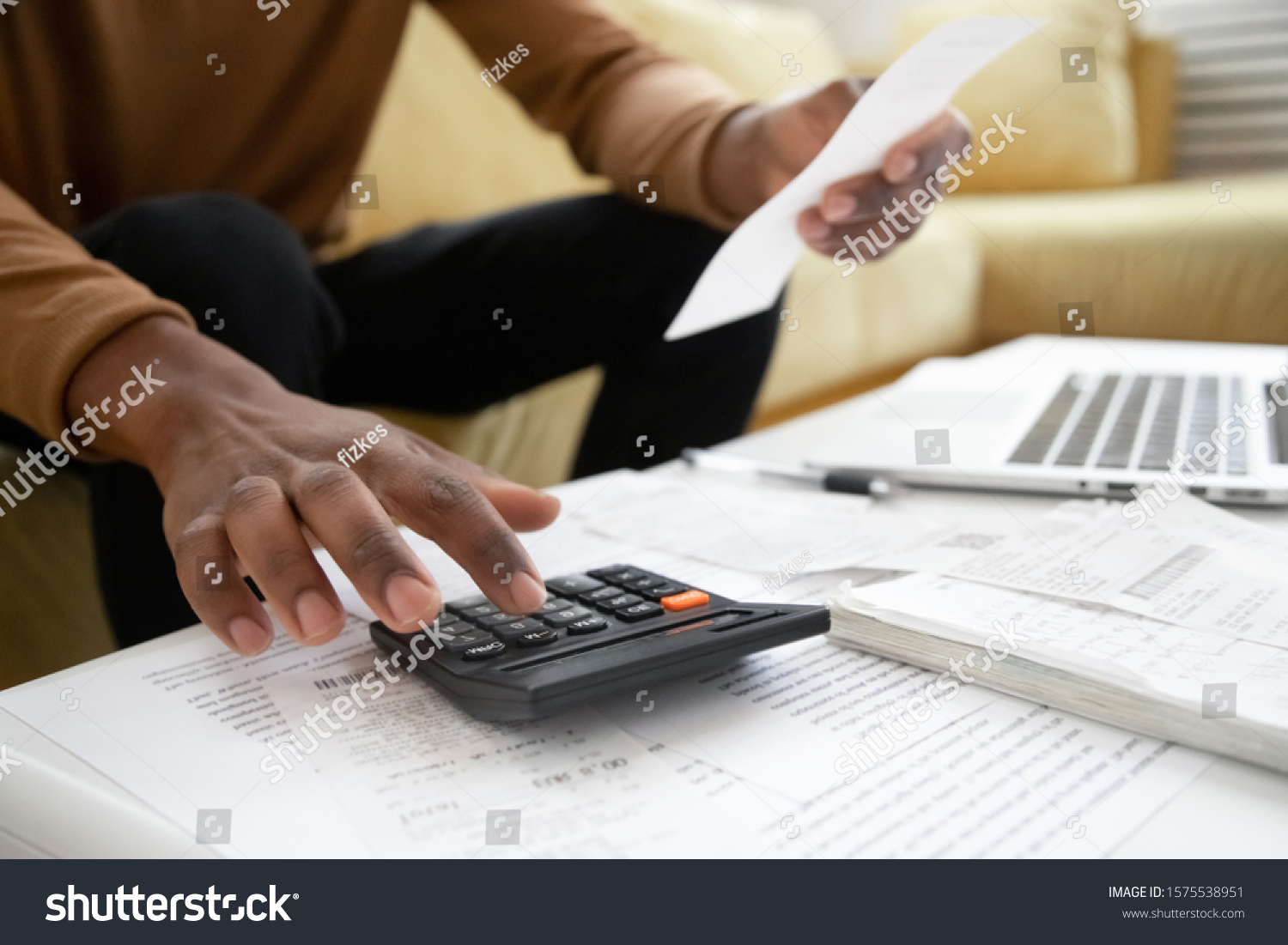 Close up of african American man calculating using machine managing household finances at home, focused biracial male make calculations on calculator paying bills, account taxes or expenses #1575538951