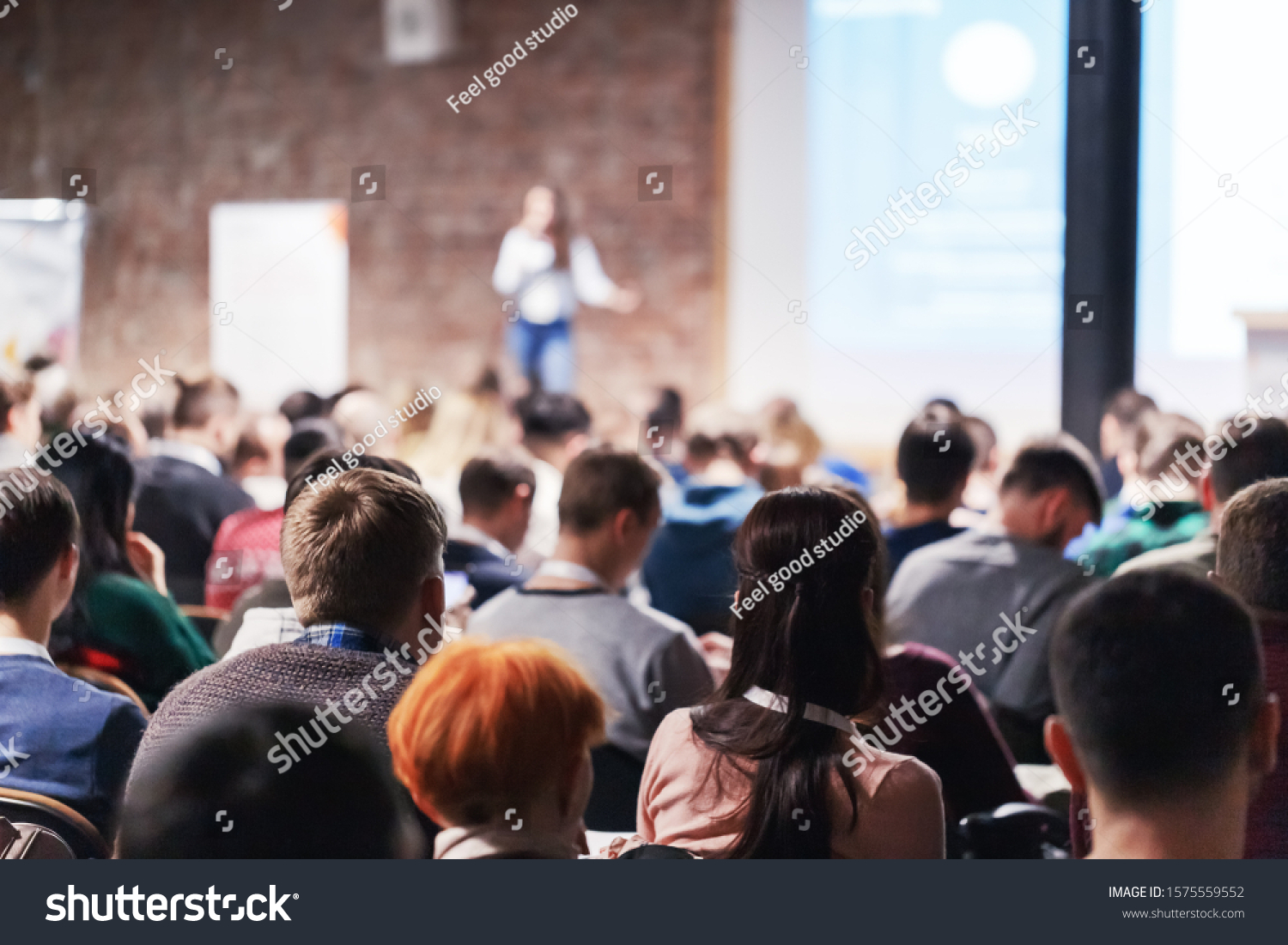 Adult people at conference listen to woman speaker providing lecture on scene in big conference hall. Business and Entrepreneurship concept. Audience at the conference hall. #1575559552
