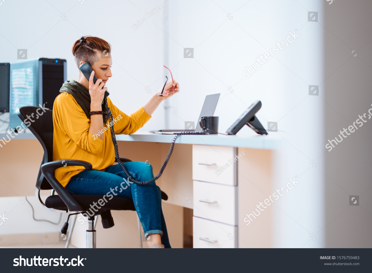 Businesswoman sitting at the desk and using landline phone in the office #1576759483