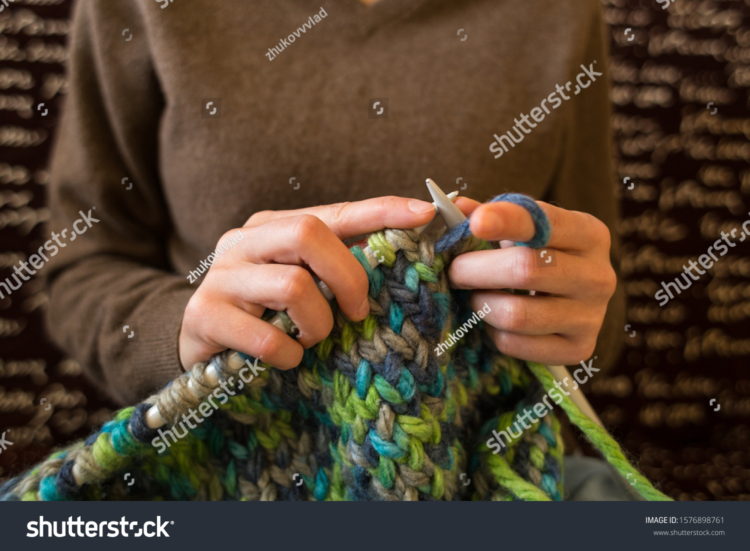 A woman knits from thick yarn. Handmade clothes. The girl sits on the couch and goes in for her hobbies. Knitting close up. Knitting needles. #1576898761