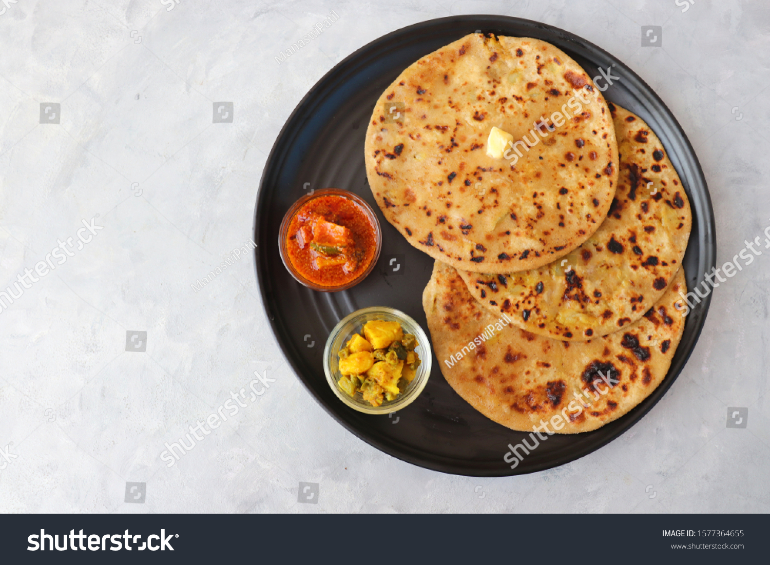 Indian Food - Aloo Paratha or Indian Potato stuffed Flatbread. Served with butter, pickle and masala potatoes. over light background with copy space. #1577364655