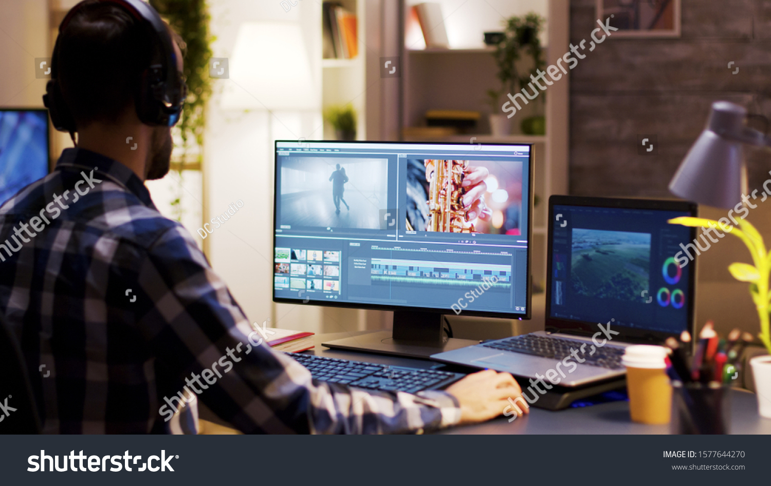 Film maker pointing at the monitor in home office while working on post production for a movie. Video editor wearing headphones. #1577644270