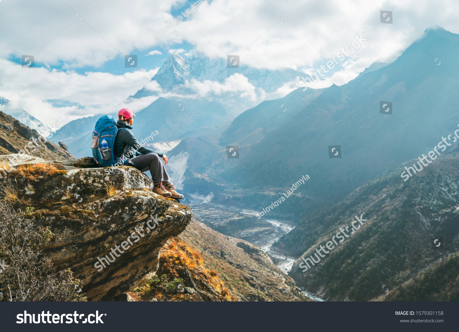 Young hiker backpacker female sitting on the cliff edge and enjoying Ama Dablam 6,812m peak view during Everest Base Camp (EBC) trekking route near Phortse, Nepal. Active vacations concept image #1579301158