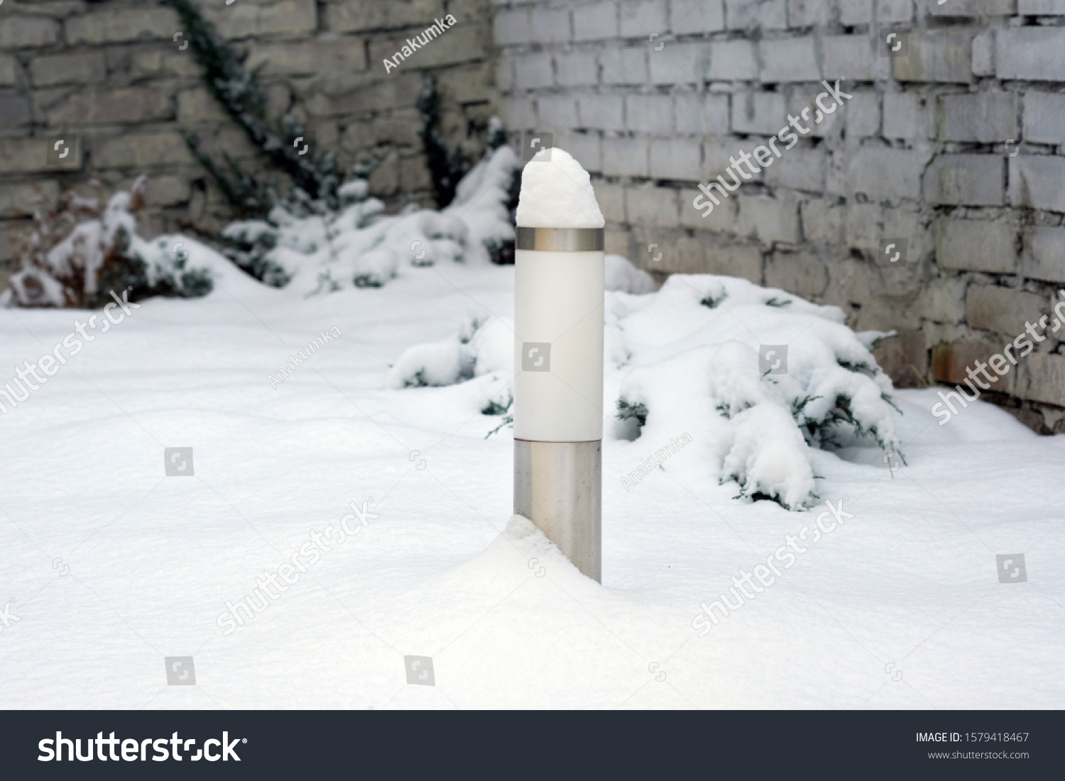 Lantern to illuminate the track at the cottage in winter. Cylindrical garden lamp on a white snow background. Solar powered LED garden park lamp. #1579418467