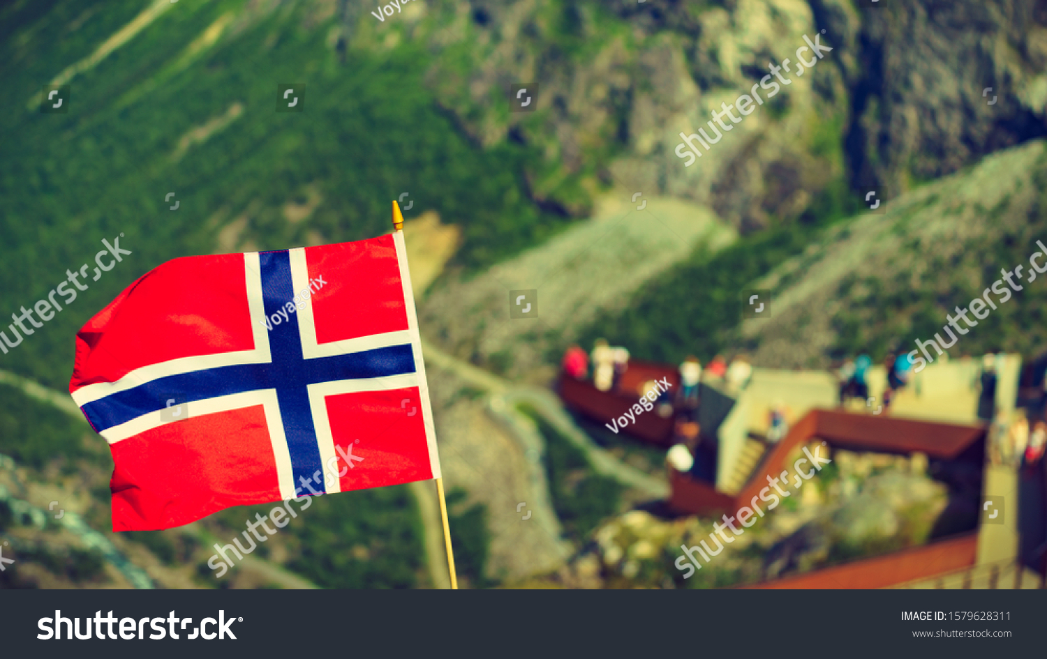 Trollstigen mountain road landscape in Norway, Europe. Norwegian flag waving and many tourists people on viewing platform in background. National tourist route. #1579628311