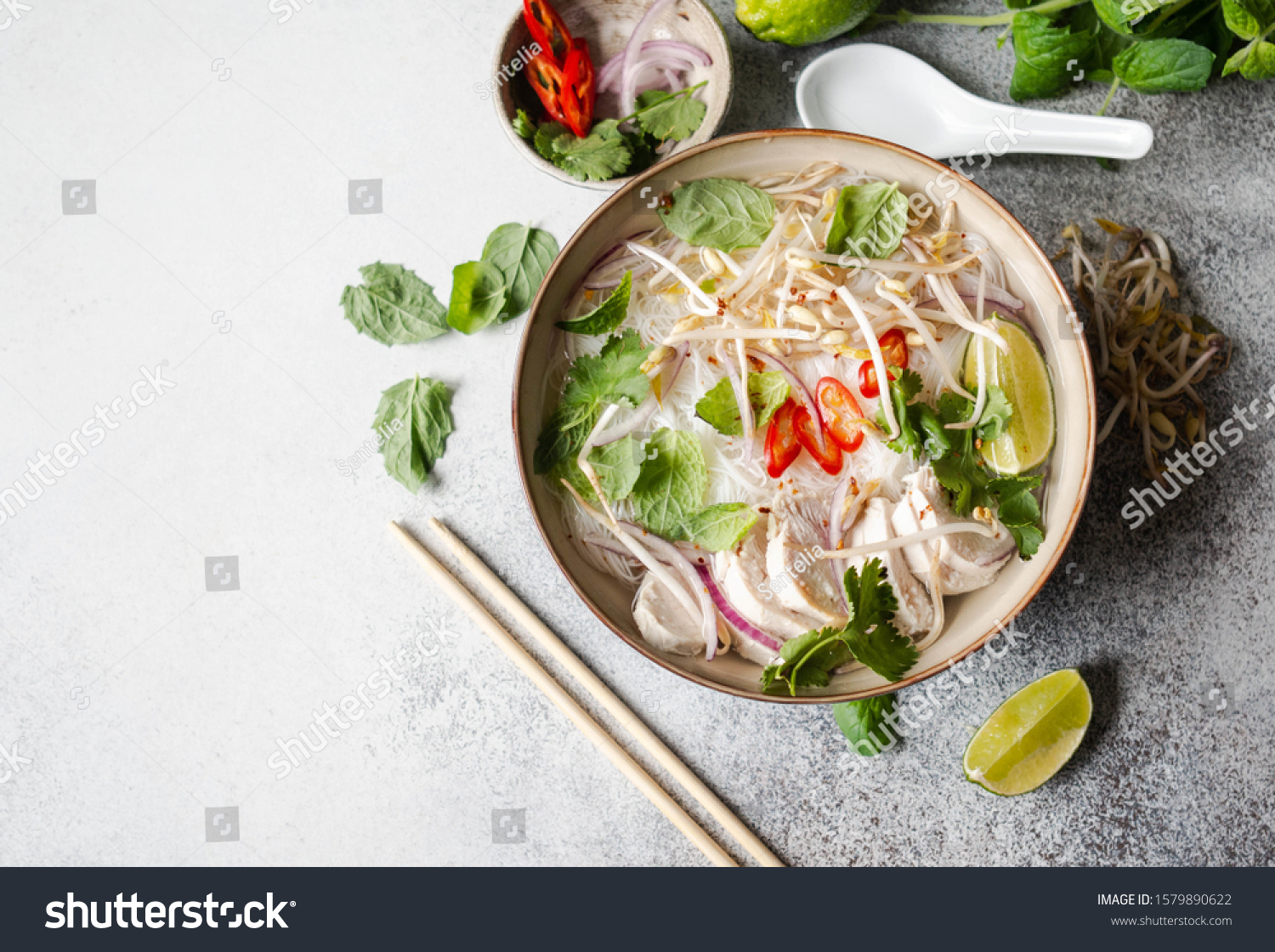 Traditional Vietnamese soup- pho ga in bowl with chicken and rice noodles, mint and cilantro, red onion, chili, bean sprouts and lime on grey background.  Asian food. Copy space. Top view  #1579890622