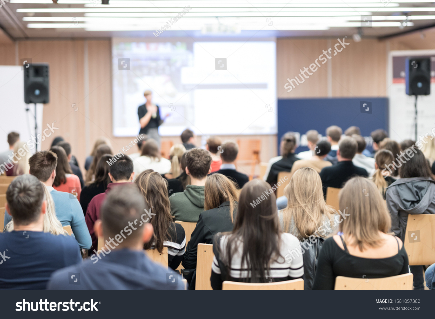 Business and entrepreneurship symposium. Female speaker giving a talk at business meeting. Audience in conference hall. Rear view of unrecognized participant in audience. #1581057382