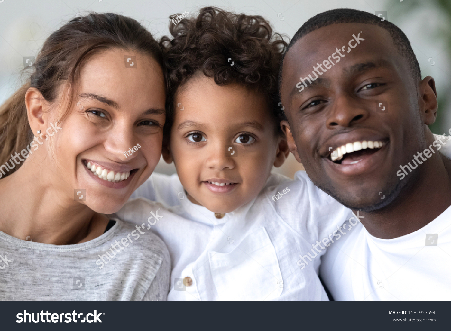 Head shot portrait close up smiling African American mother, father and son with healthy white smiles, happy family posing for photo, looking at camera, cute little child embracing parents #1581955594