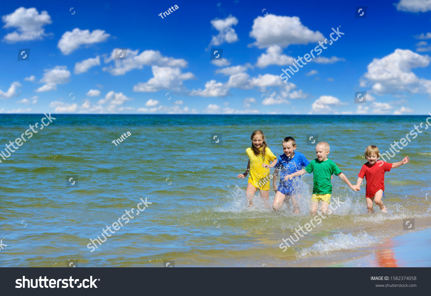 Two girls and two boys in colorful t-shirts running on a sandy beach, blue sky white clouds in the background #1582374058