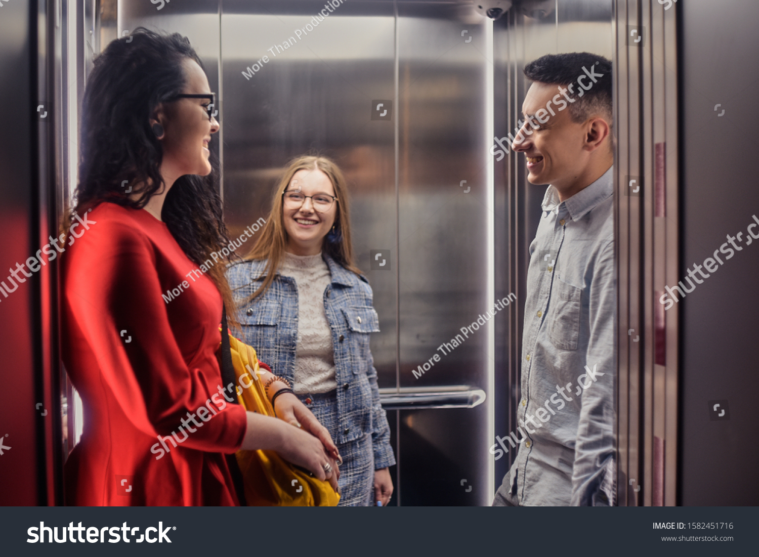 The girls and the guy ride in the elevator. Students go to study. People in the elevator. Elevator with people, communication in public places. Colleagues go to work in the elevator. #1582451716