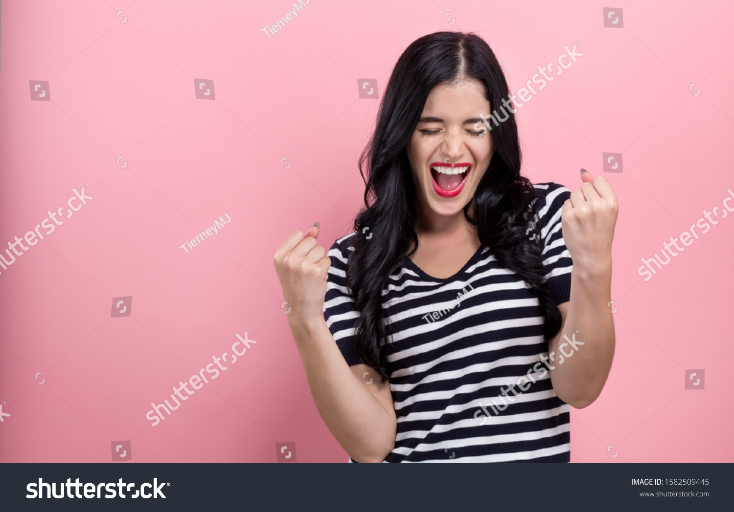 Happy young woman making a yay gesture on a pink background #1582509445