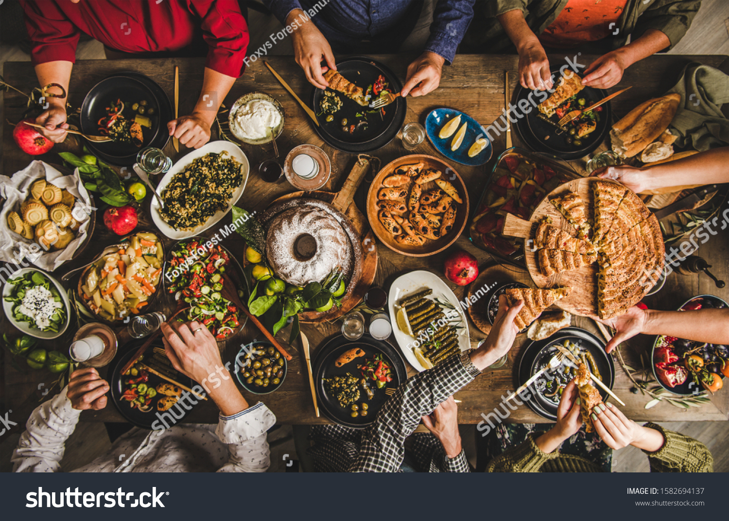 Traditional Turkish family celebration dinner. Flat-lay of people eating Turkish salads, cooked vegetables, meze starters and borek pie and drinking raki drink, top view. Middle Eastern cuisine #1582694137
