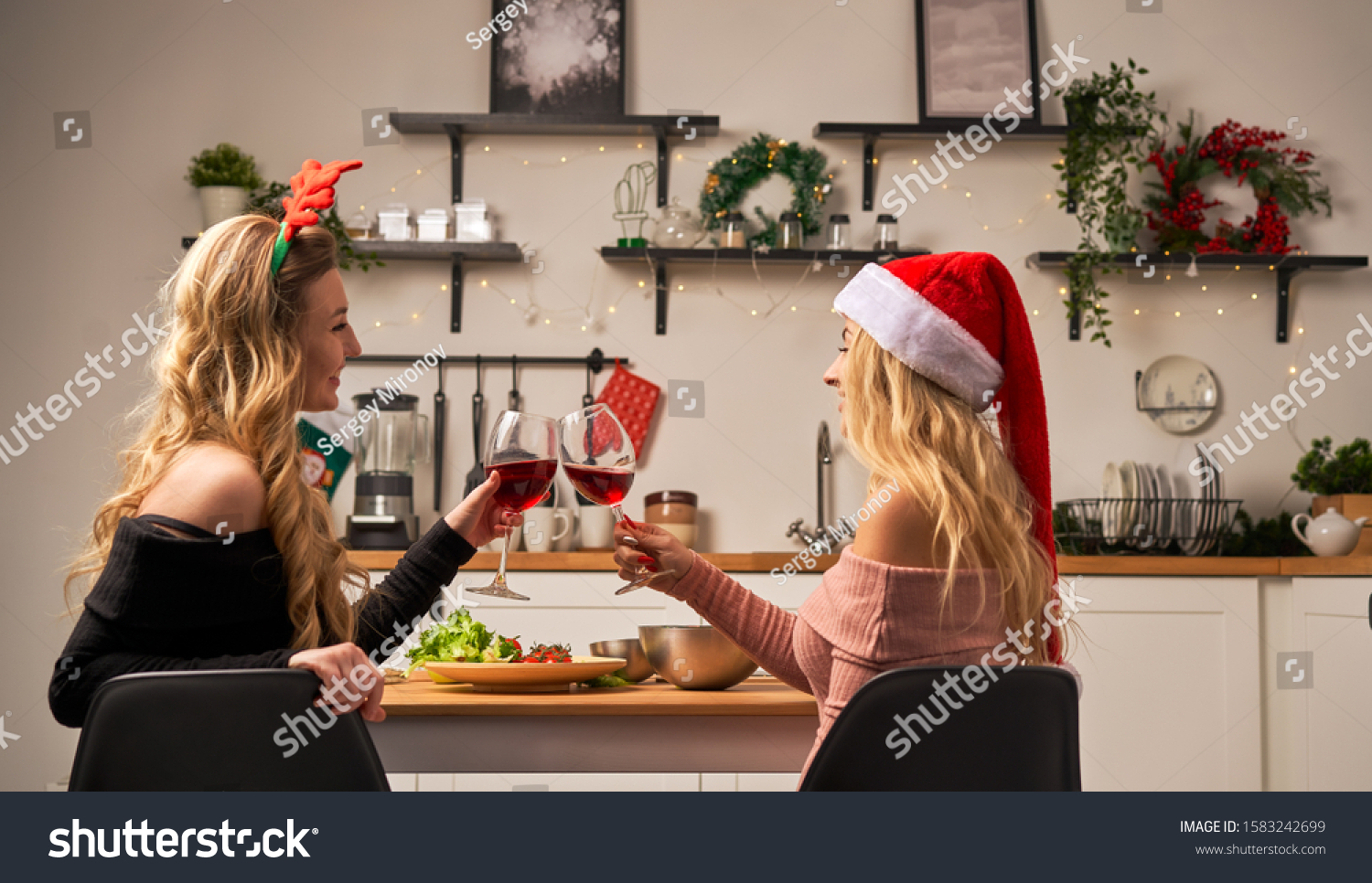 Two women sitting at festive table with wine glasses in kitchen at Christmas. #1583242699