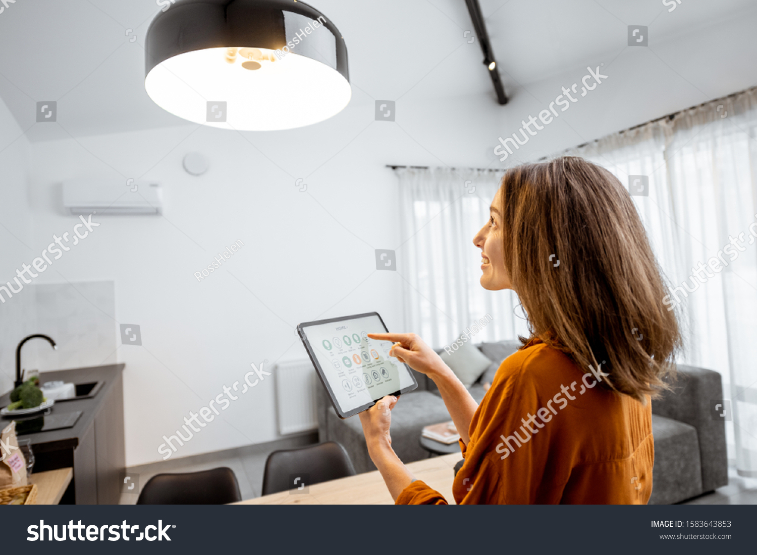 Young woman controlling home light with a digital tablet in the living room. Concept of a smart home and light control with mobile devices #1583643853
