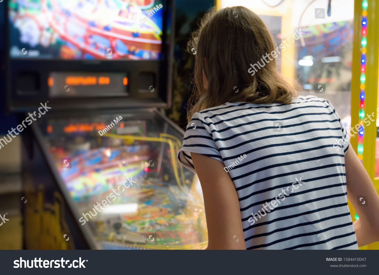 Little girl playing pinball game in theme park. #1584410047