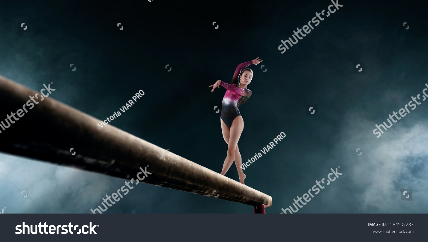 Female gymnast doing a complicated trick on gymnastics balance beam. #1584507283
