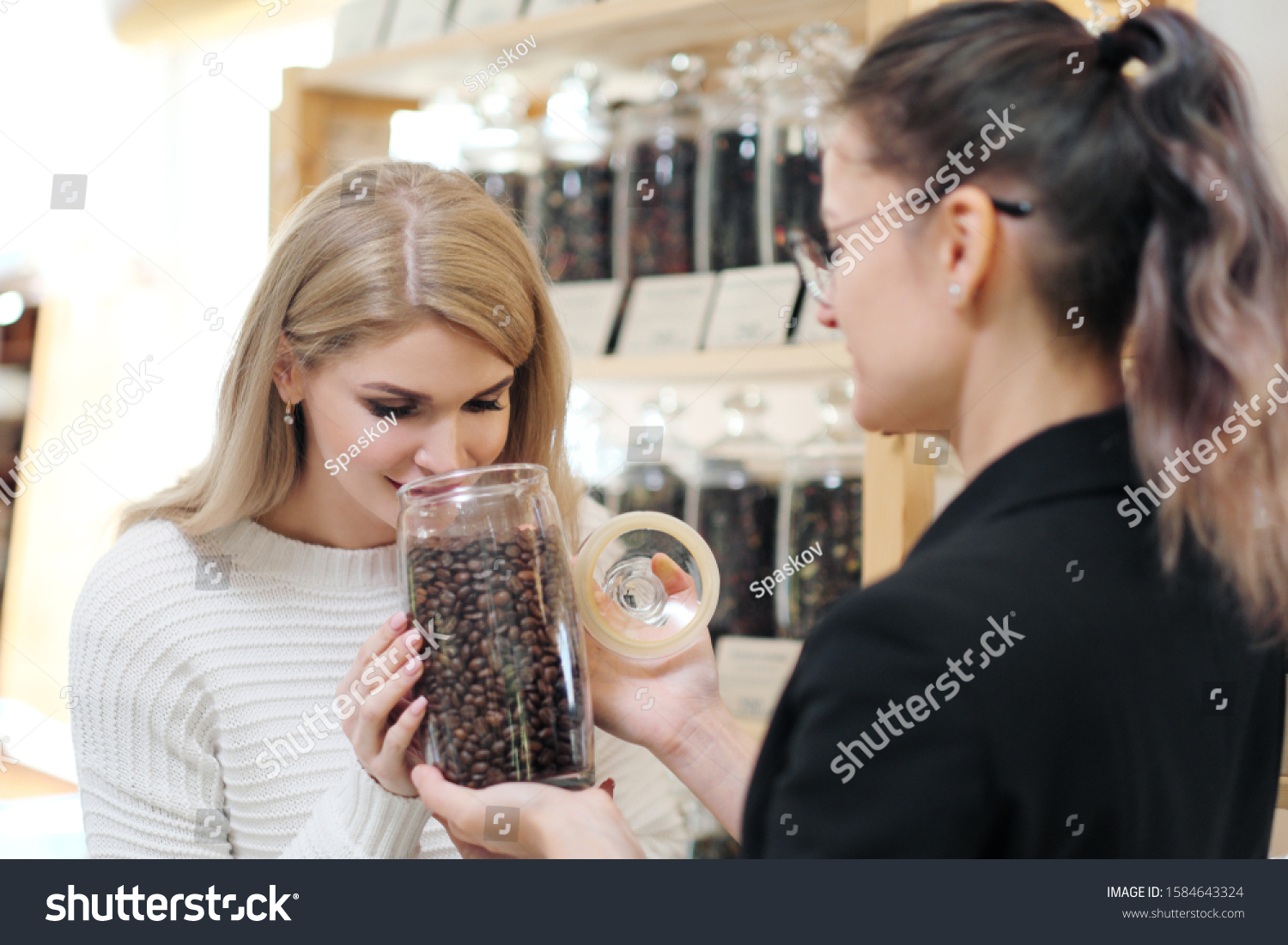 A female shopper in the store chooses a grain coffee. The seller helps the buyer choose. #1584643324