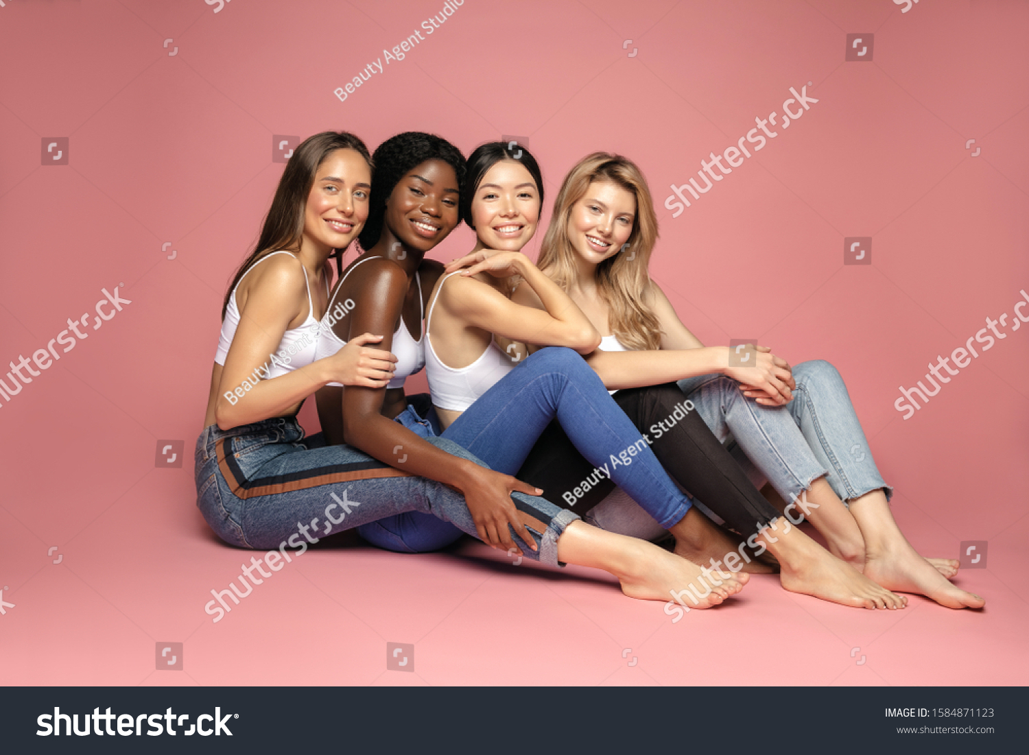 Multi Ethnic Group of Womans with diffrent types of skin sitting together and looking on camera. Diverse ethnicity women - Caucasian, African and Asian against pink background #1584871123