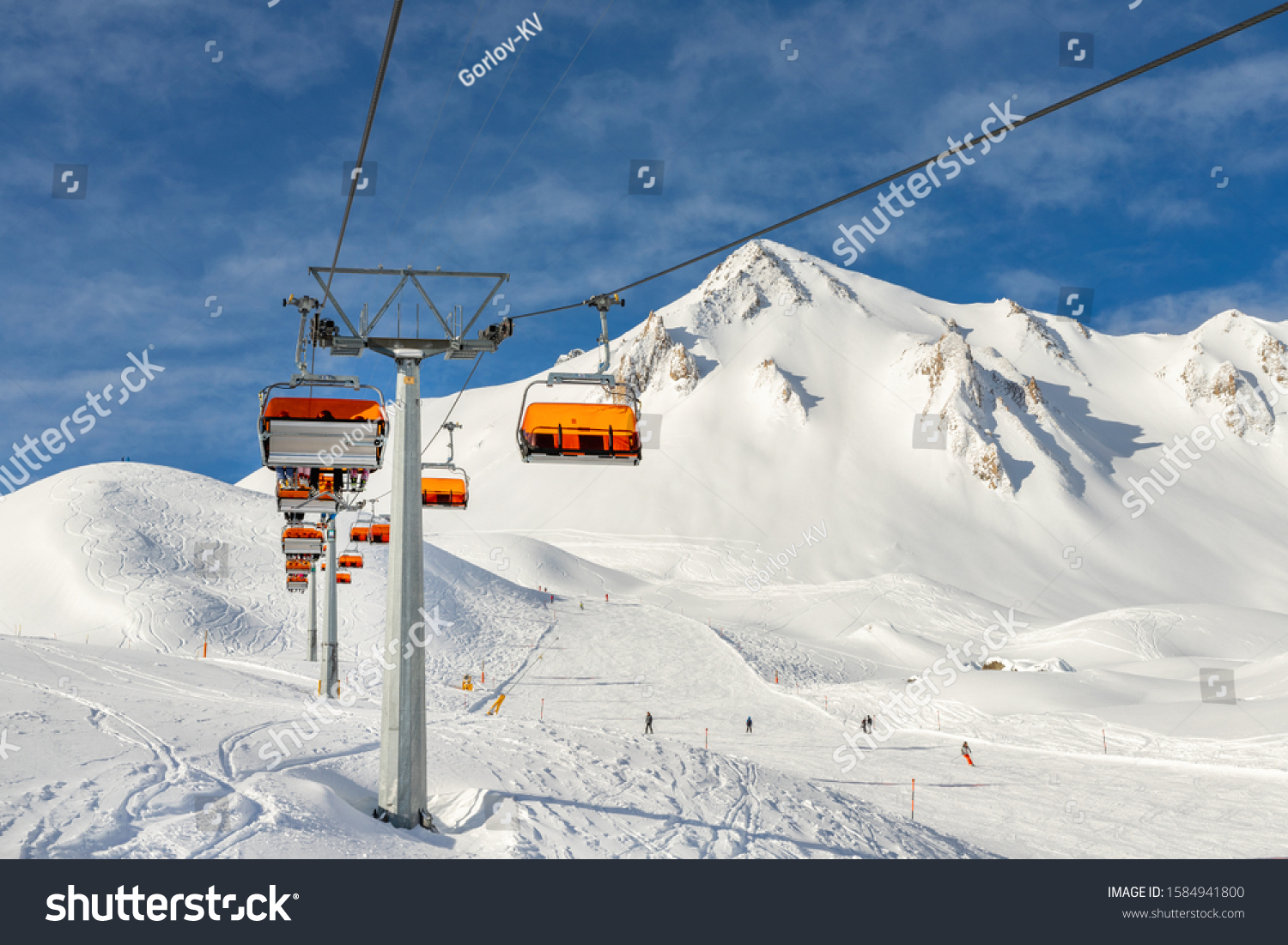 Ski lift ropeway on hilghland alpine mountain winter resort on bright sunny day. Ski chairlift cable way with people enjoy skiing and snowboarding.Banner panoramic wide view of downhill slopes #1584941800