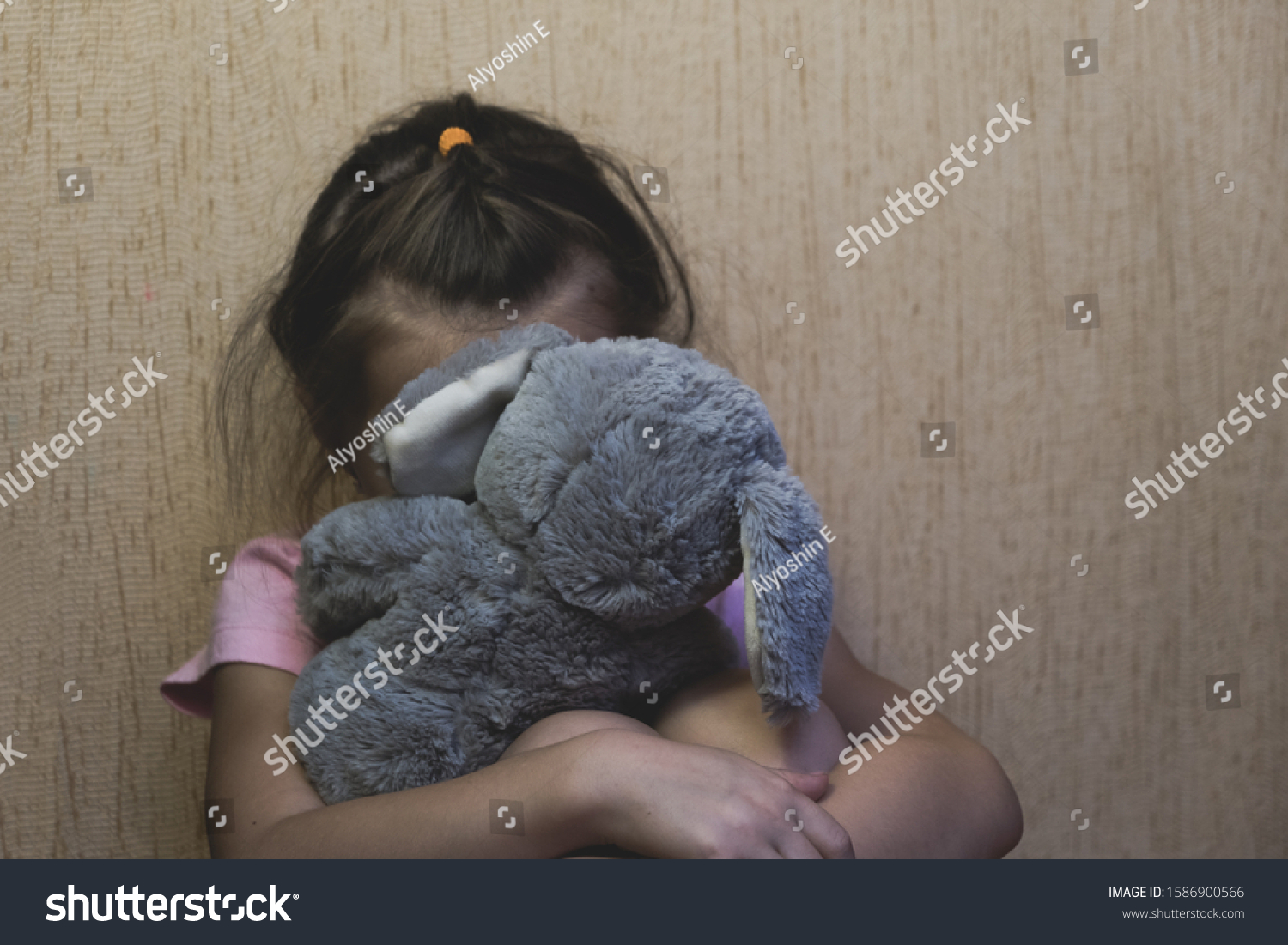 Depressed child sitting and hidden behind her toy teddy bear. domestic and violence, beaten sitting at the wall, Domestic violence. Copy space. #1586900566