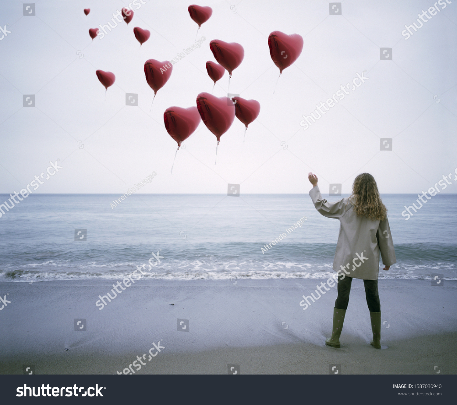 View of a woman letting heart-shaped balloons go on the beach #1587030940
