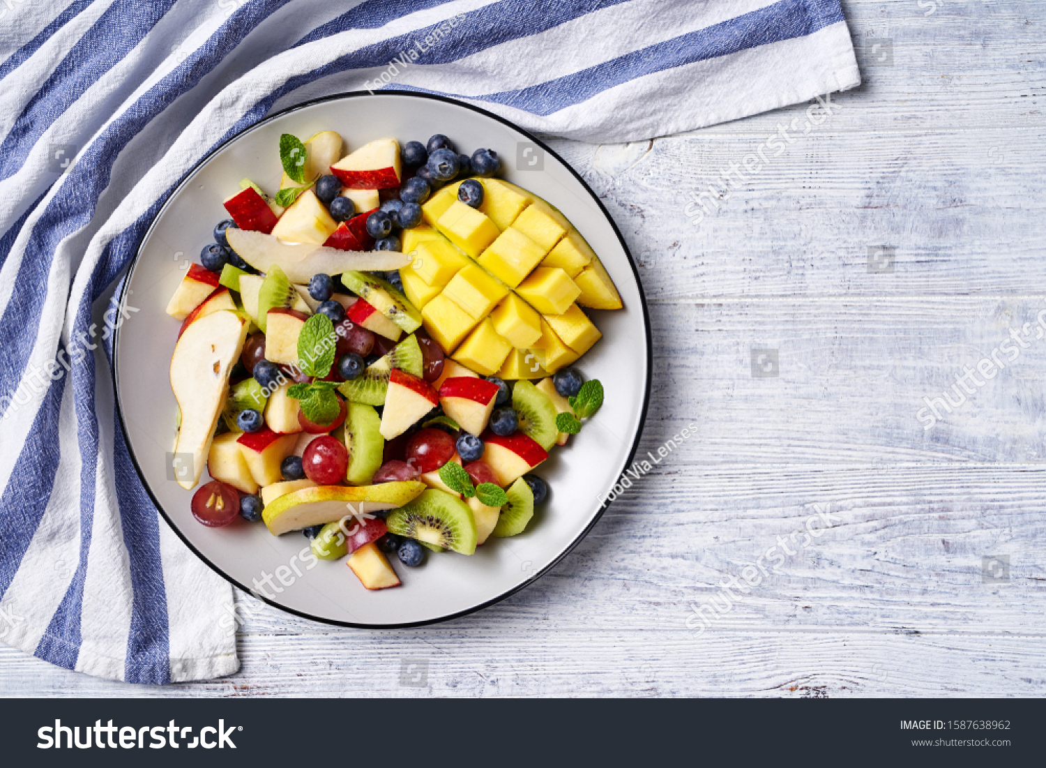 Fruit salad on a plate of mango, blueberries, red grape, pears, apple, with fresh mint, on a white wooden table, horizontal view, copy space, copy space #1587638962
