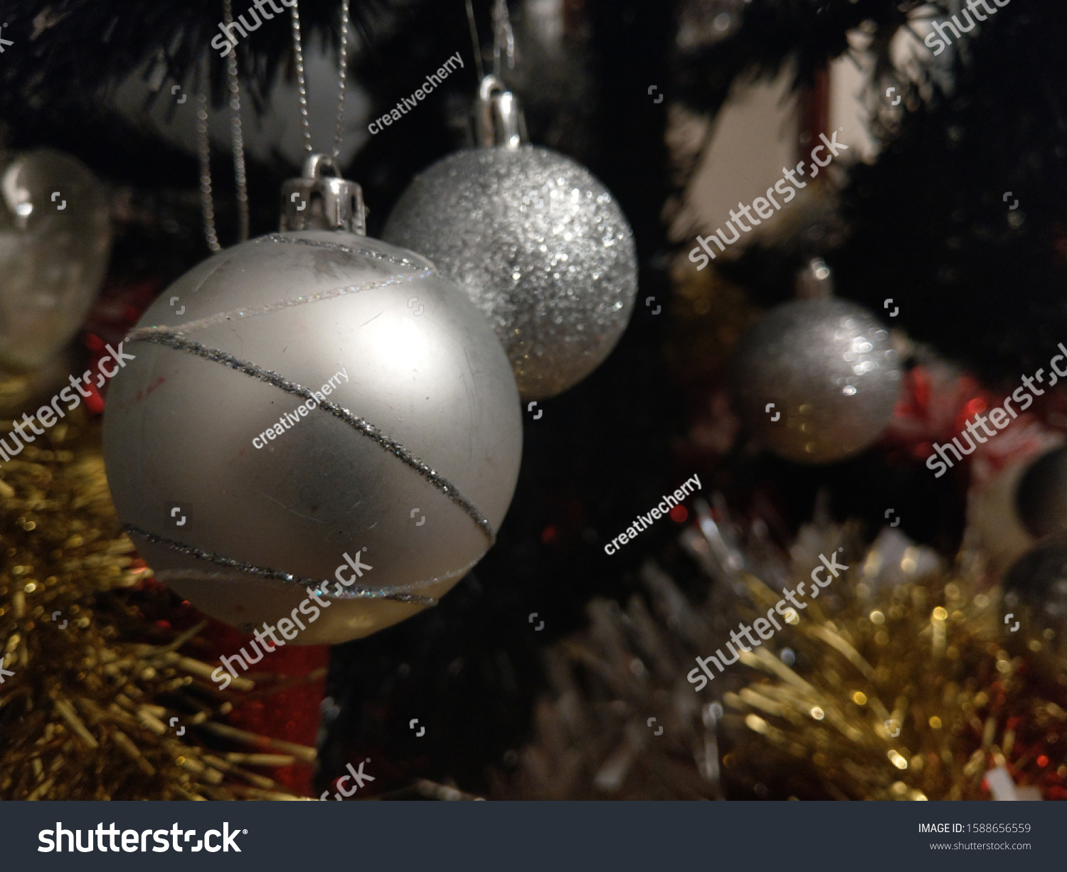 silver bauble infront of other baubles hanging on a tree with gold and red tinsel in view #1588656559