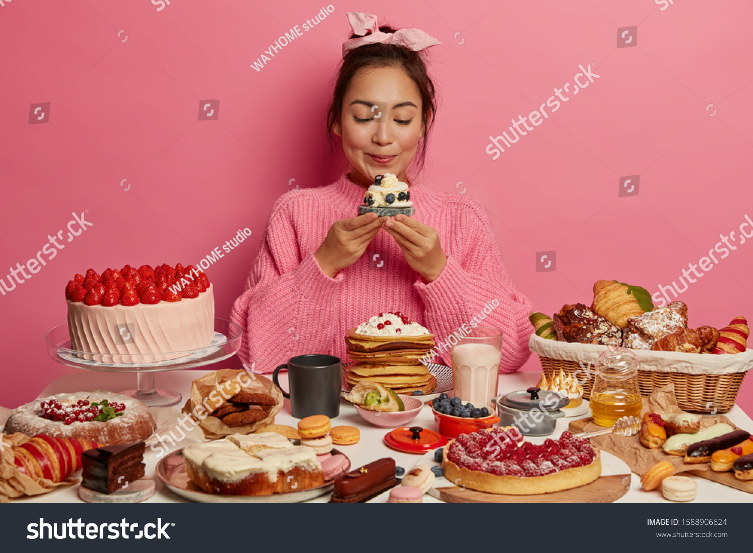Photo of adorable Korean woman holds yummy sugary dessert or muffin, isolated over pink background, tastes fresh baked confectionery, cant imagine life without sweet dishes, dressed casually #1588906624