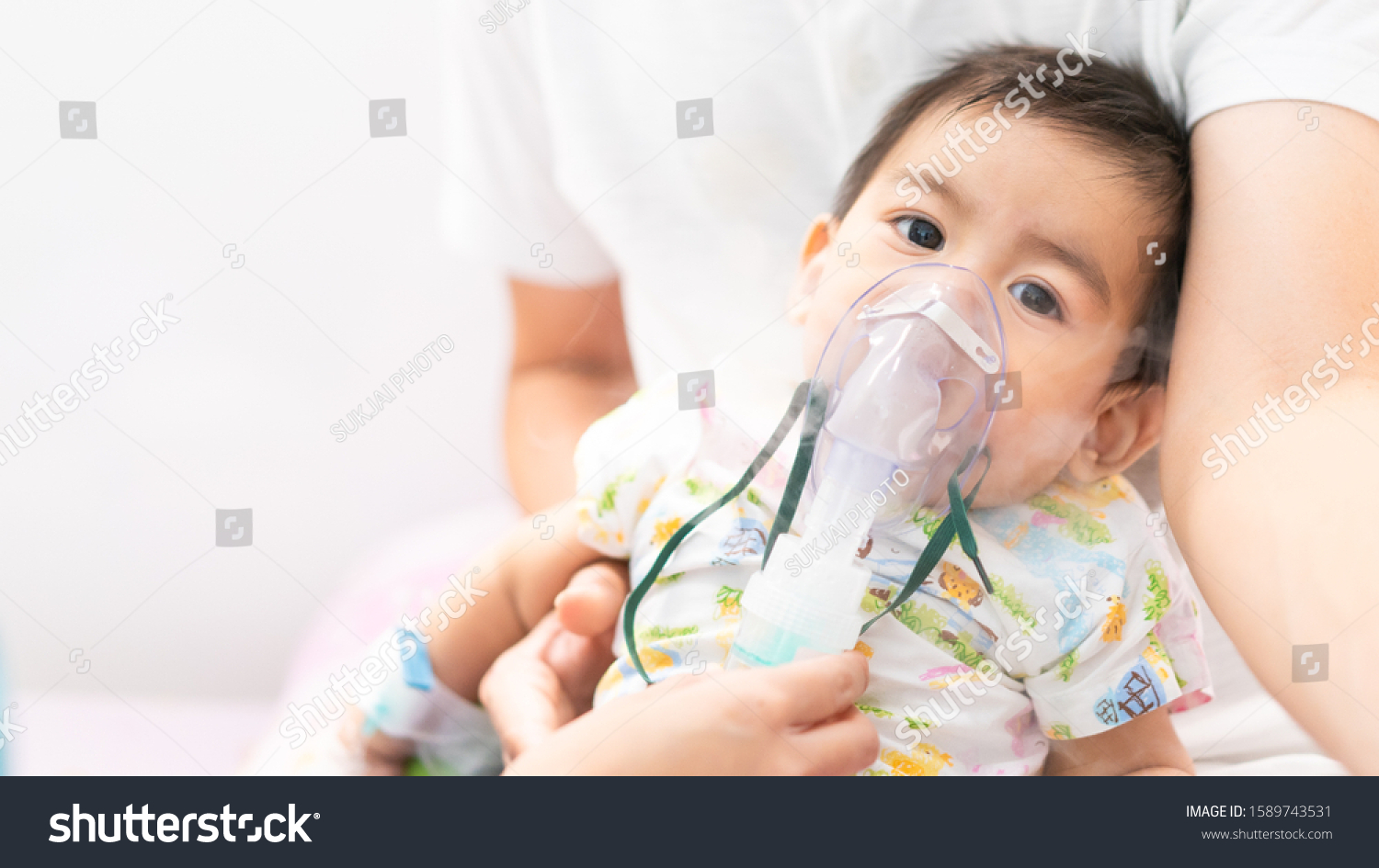 Close up of asian little baby boy is treated respiratory problem with vapor nebulizer to relief cough symptom in the hospital room , concept of pediatric patient care for sick in the hospital. #1589743531