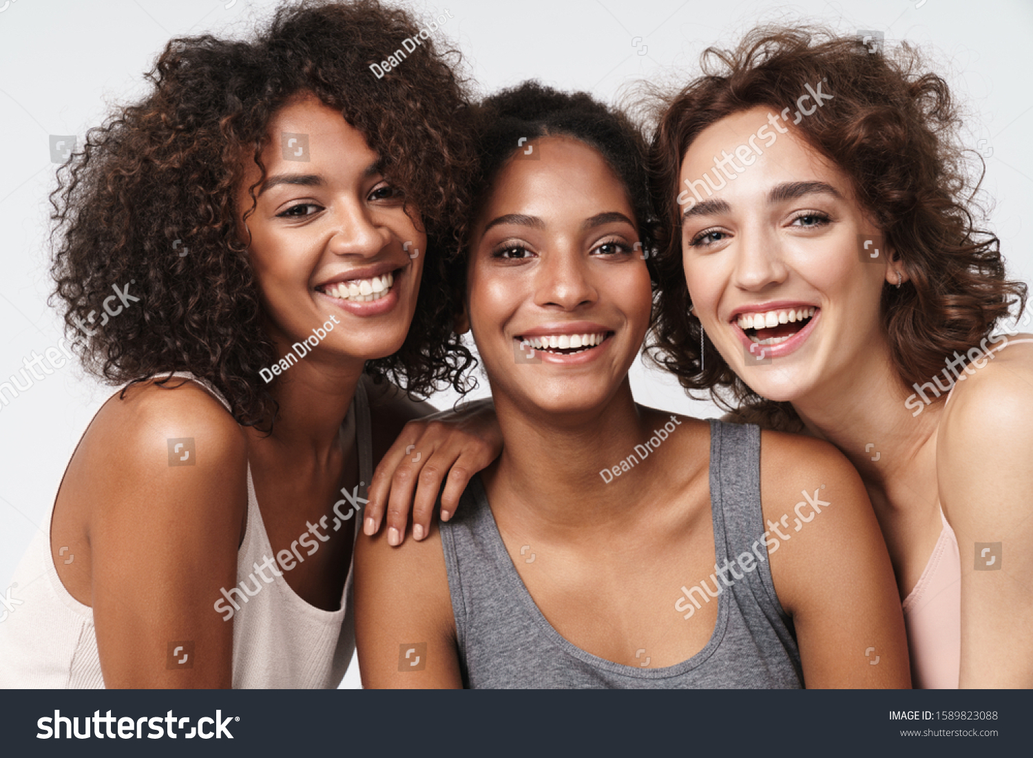 Portrait of three young multiracial women standing together and smiling at camera isolated over white background #1589823088