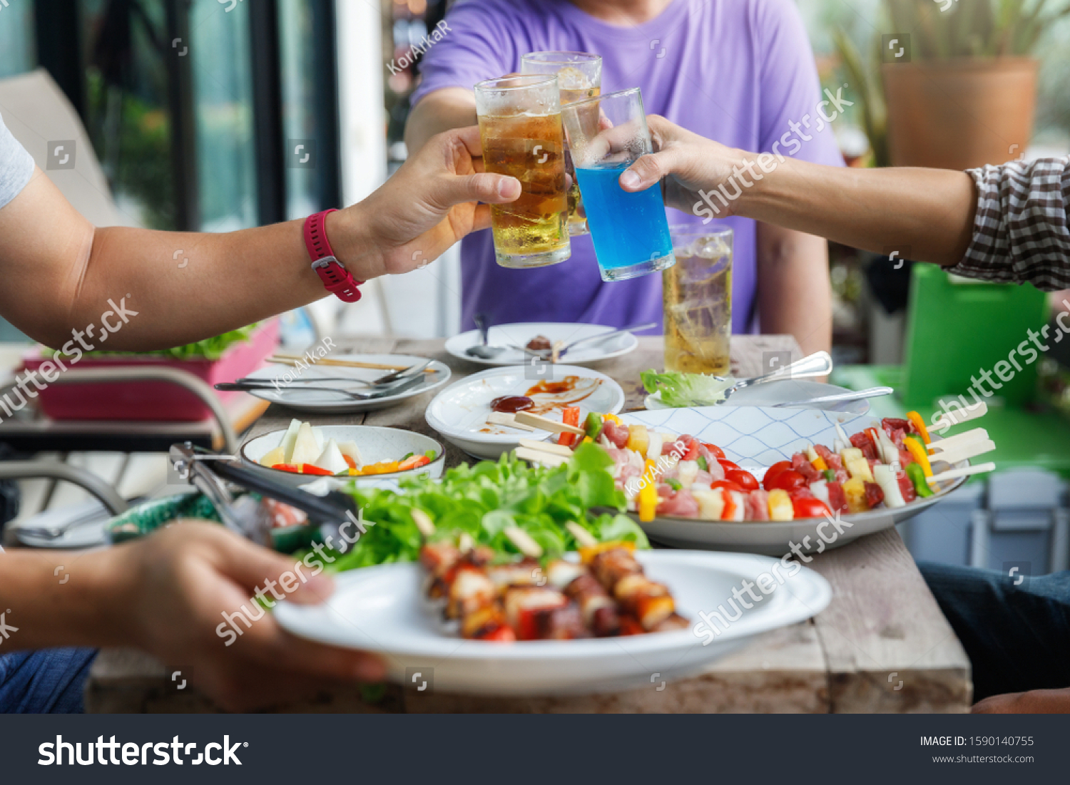 Young men cheers for a drink at a BBQ party between friends. Food, drink, people and family time concept. #1590140755