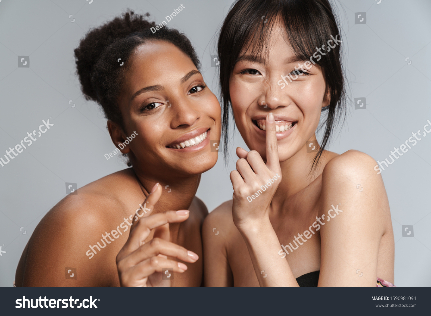 Portrait of two multinational half-naked women making silence gesture and smiling isolated over grey background #1590981094