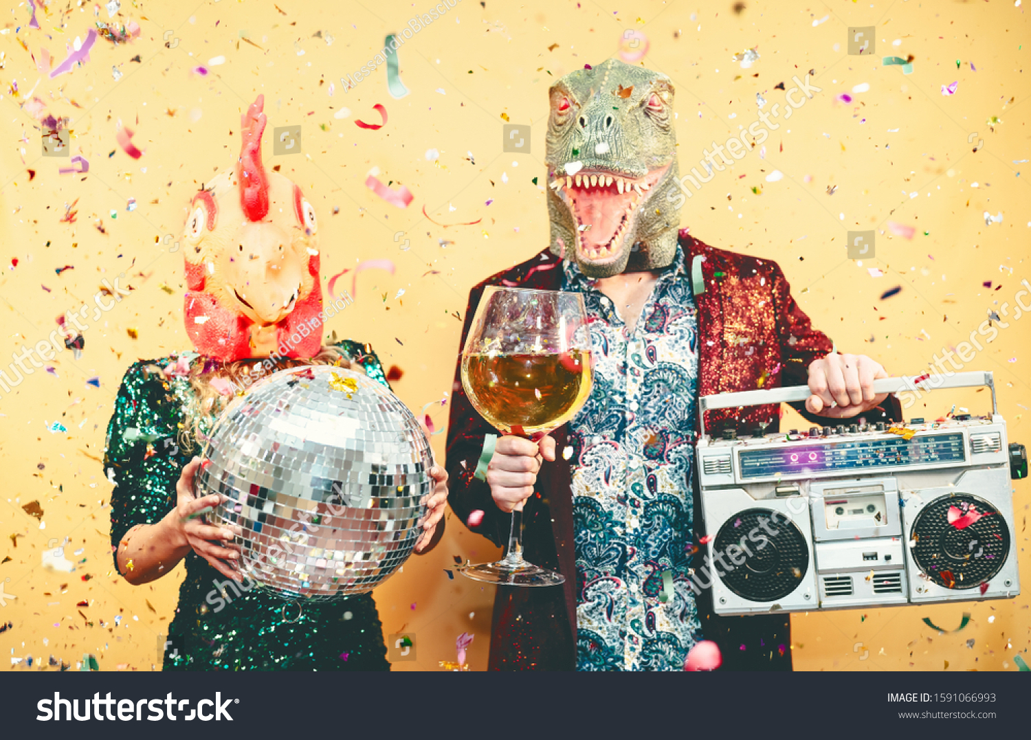 Crazy couple celebrating new year eve wearing chicken and dinosaur t-rex mask - Young trendy people having fun drinking champagne and listening music with vintage boombox - Absurd and holidays concept #1591066993