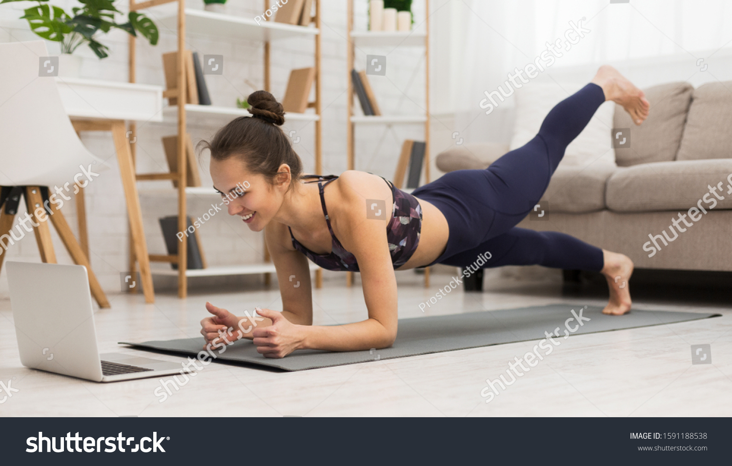 Fit woman doing yoga plank and watching online tutorials on laptop, training in living room #1591188538