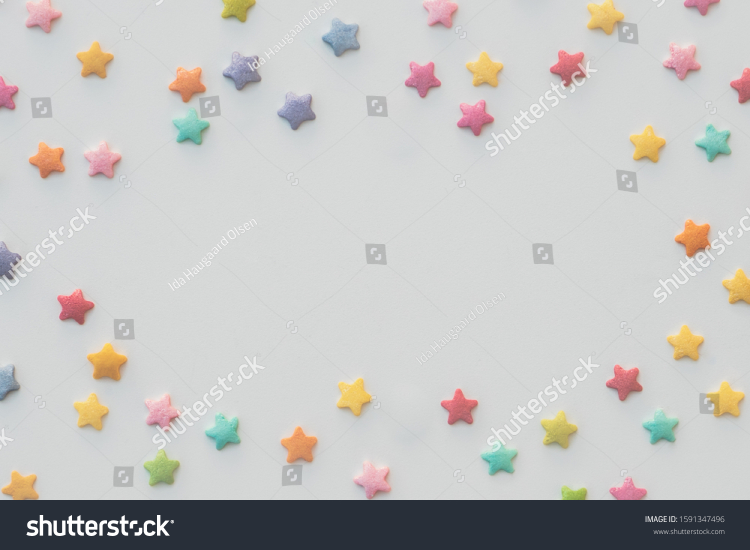 Colorful stars of sprinkles placed as a frame on white background. Room for text or placing an object in the middle. #1591347496