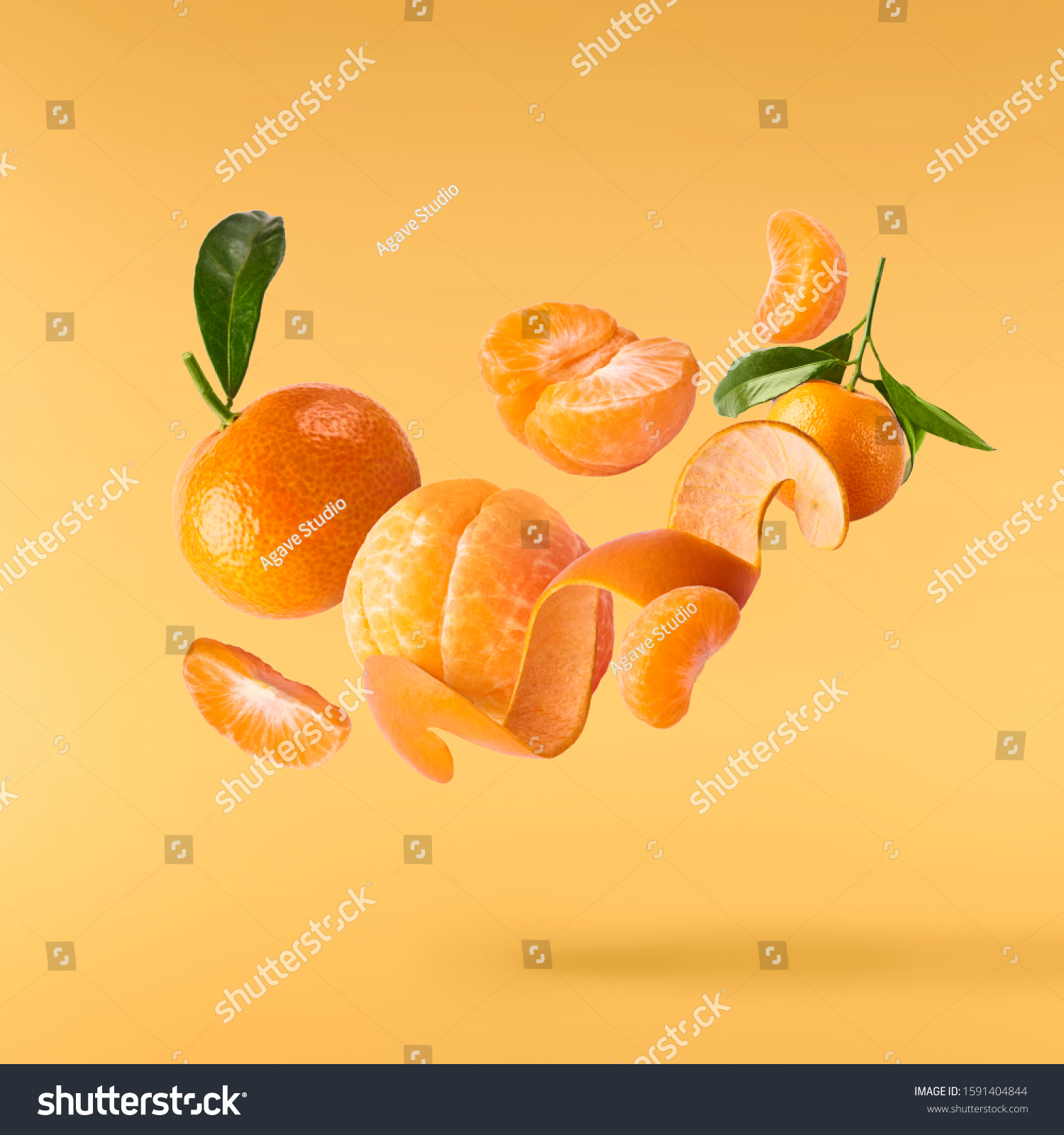 Fresh ripe mandarine with leaves falling in the air. Cut and whole mandarine isolated on yellow background. Food levitation concept. High resolution image #1591404844