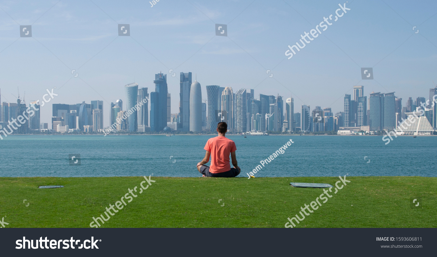 A man meditates and relaxes on the hill of the MIA park in Doha Qatar over looking the city skyline #1593606811