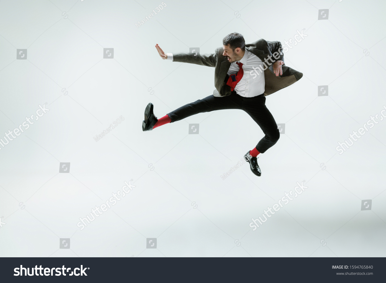 Young caucasian man moving flexible on white studio background. Male model in office attire bending over, avoiding something, catched in motion and action. Looks angry, scared, fighting. Emotions. #1594765840