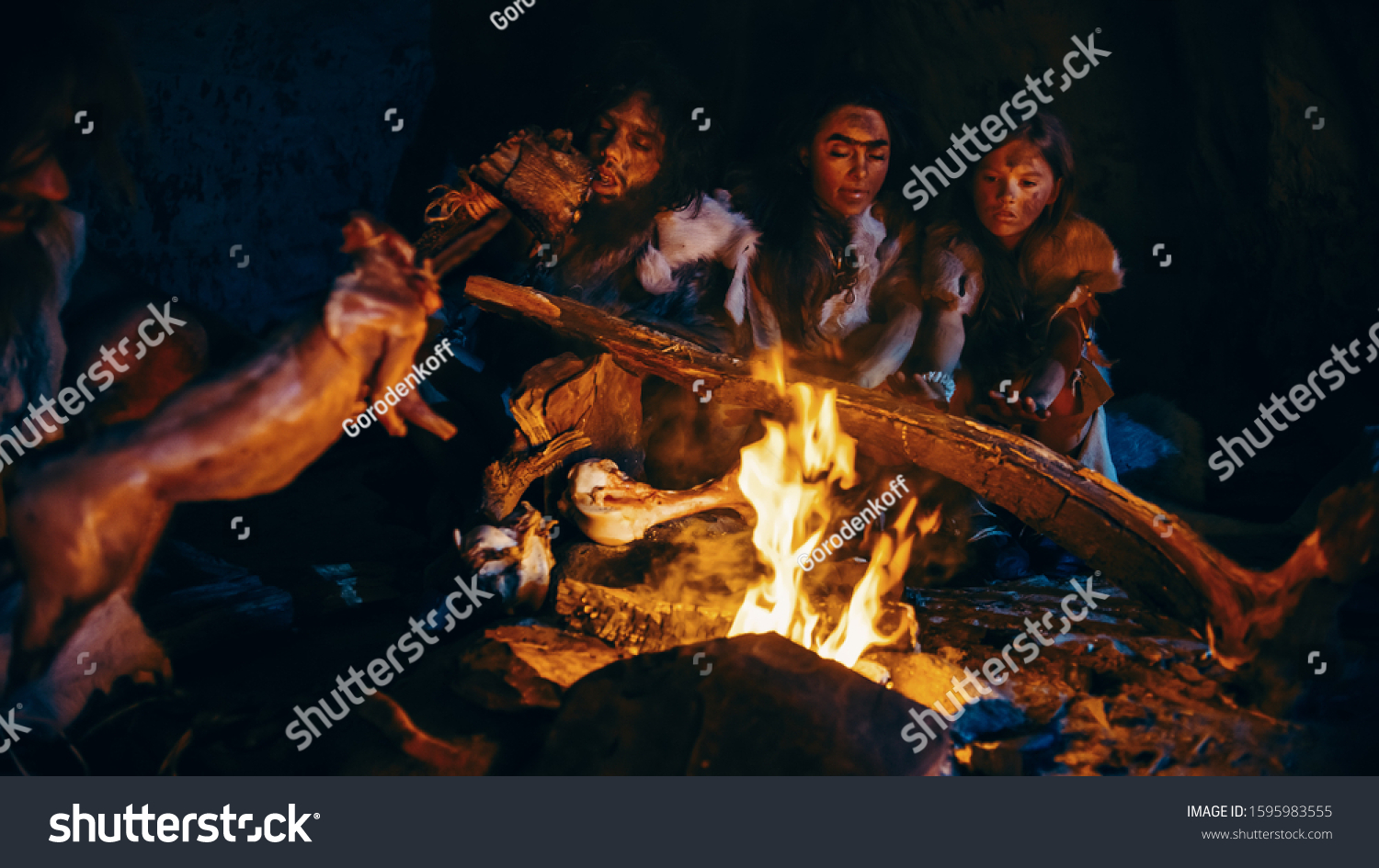 Neanderthal or Homo Sapiens Family Cooking Animal Meat over Bonfire and then Eating it. Tribe of Prehistoric Hunter-Gatherers Wearing Animal Skins Eating in a Dark Scary Cave at Night #1595983555