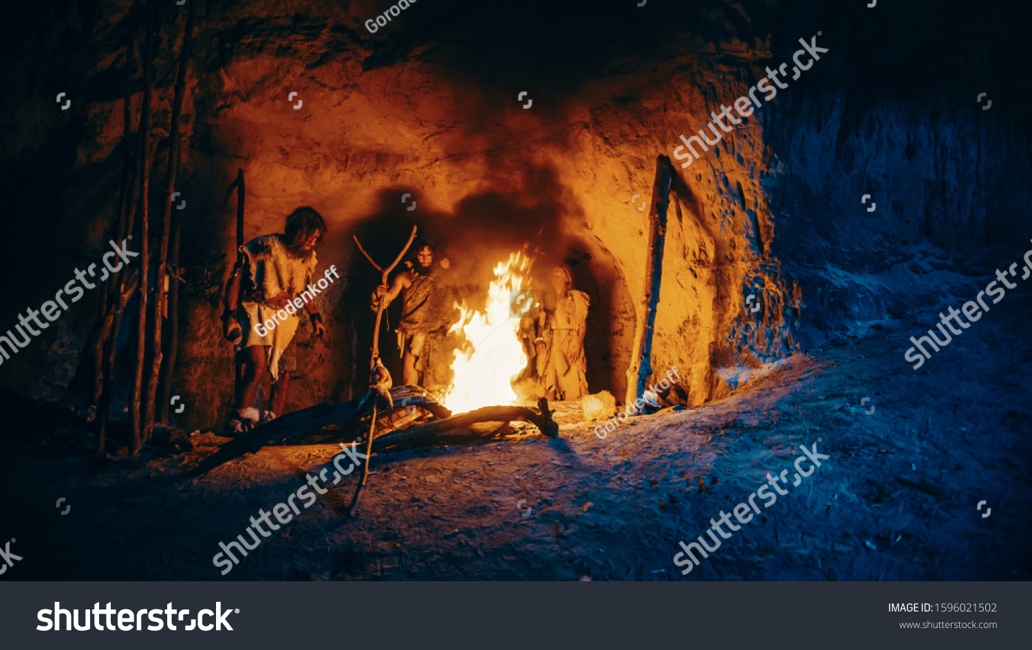 Tribe of Prehistoric Hunter-Gatherers Wearing Animal Skins Stand Around Bonfire Outside of Cave at Night. Portrait of Neanderthal / Homo Sapiens Family Doing Pagan Religion Ritual Near Fire #1596021502