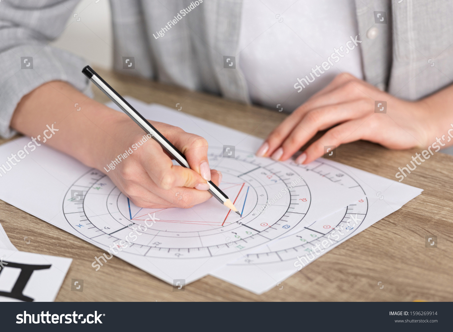 Cropped view of astrologer drawing natal chart on wooden table #1596269914