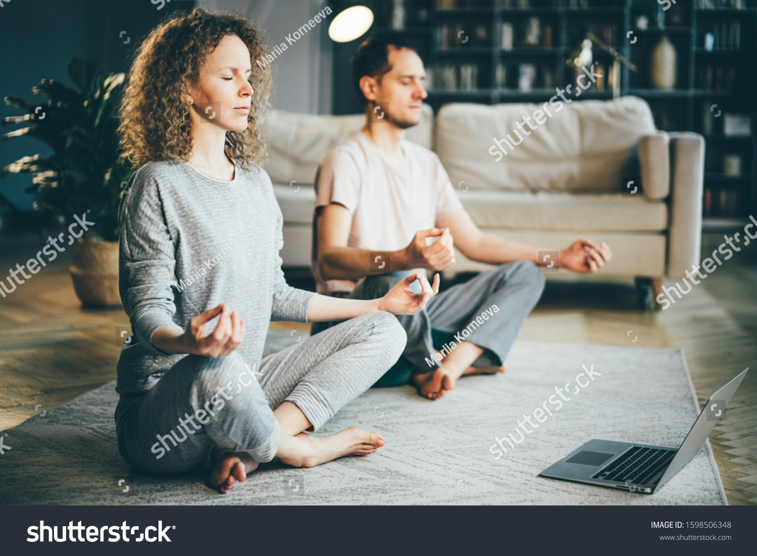 Calm couple in pajamas meditating, listening spiritual practices lessons on laptop, sitting on lotus pose at home. Yoga concept. #1598506348