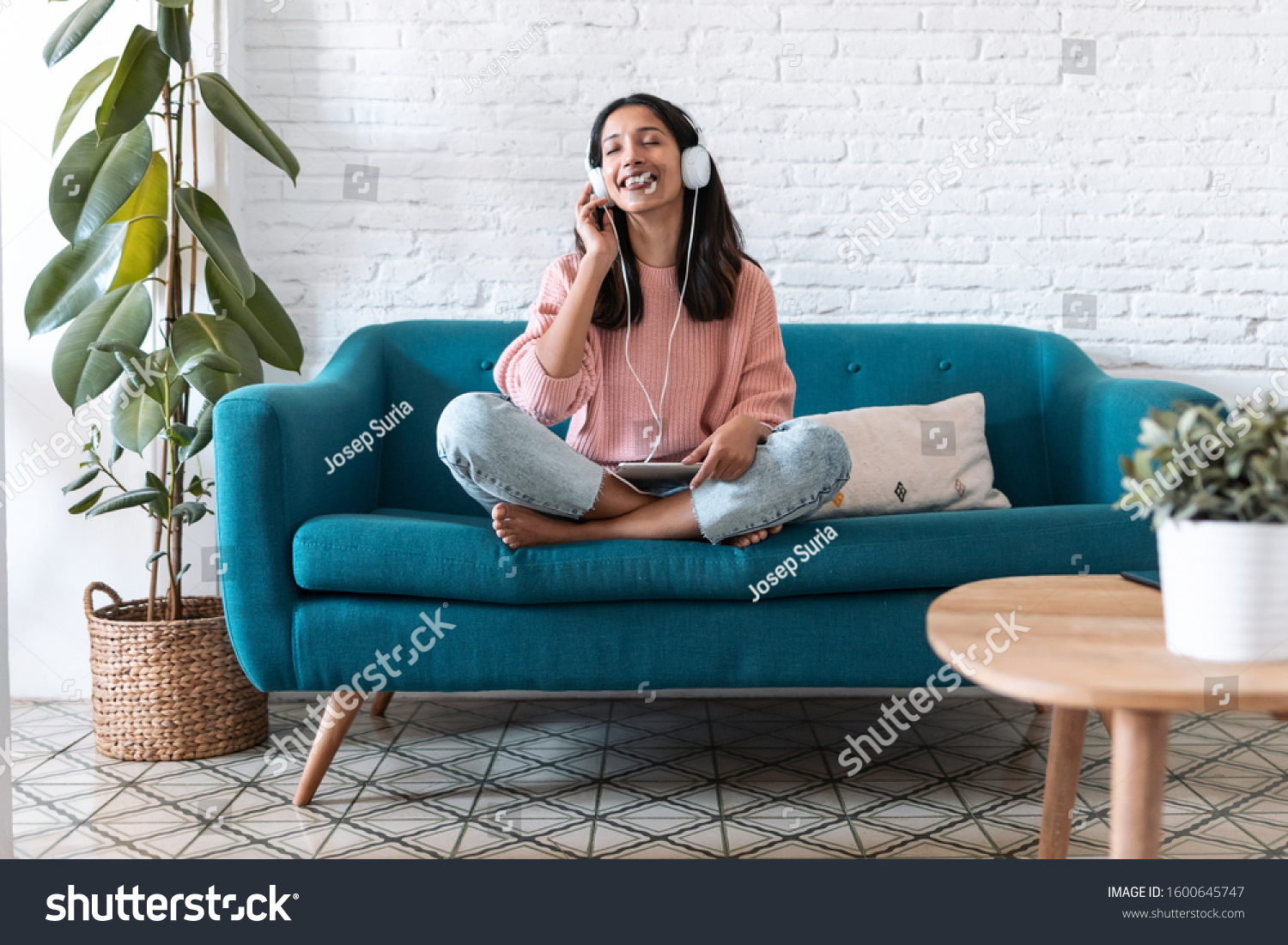 Shot of pretty young woman listening to music with digital tablet and relaxing while sitting on sofa at home. #1600645747