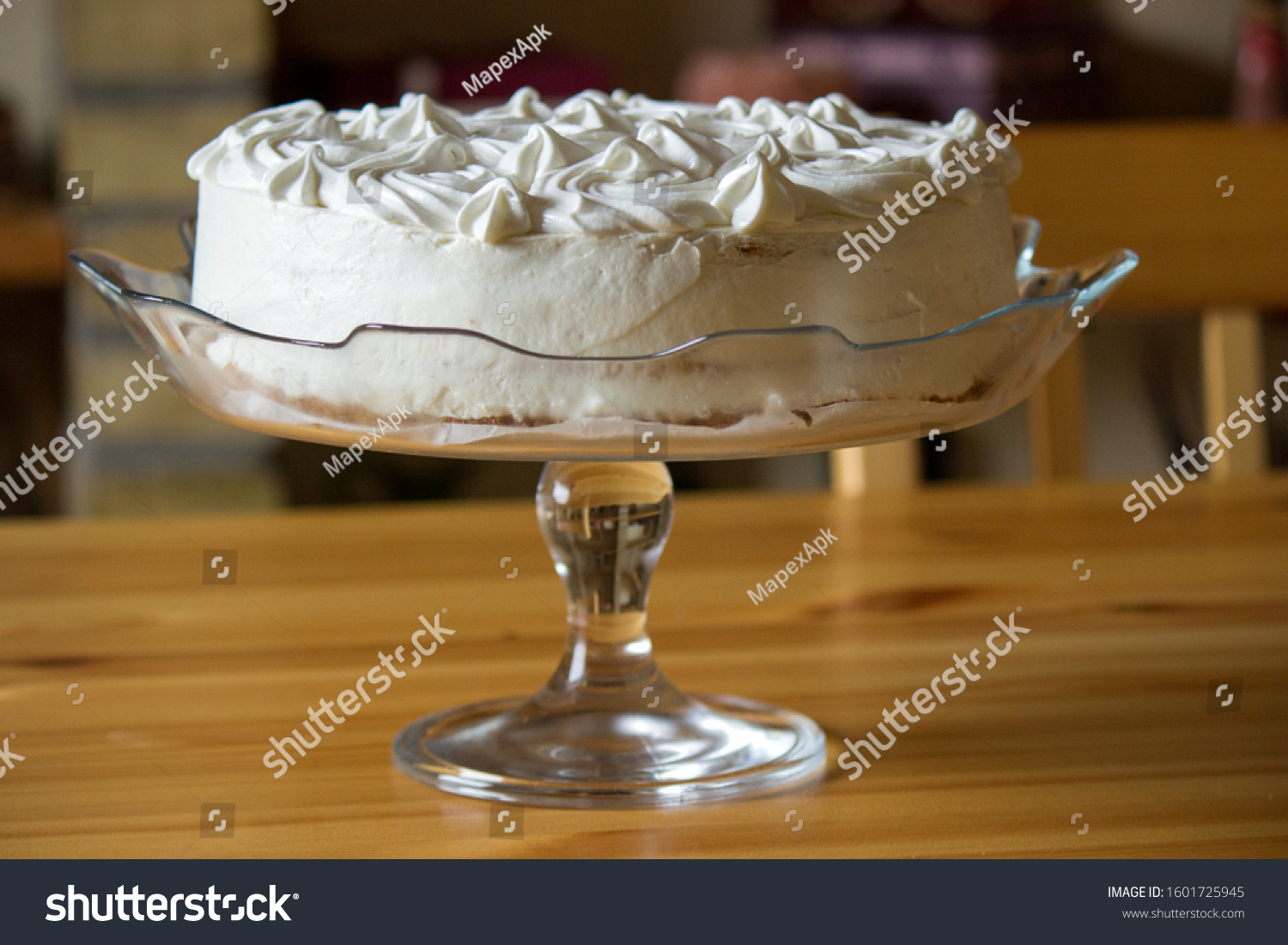 Front look Of A White Frosted Cake Placed On A Glass Plate.Wooden Table Below. #1601725945