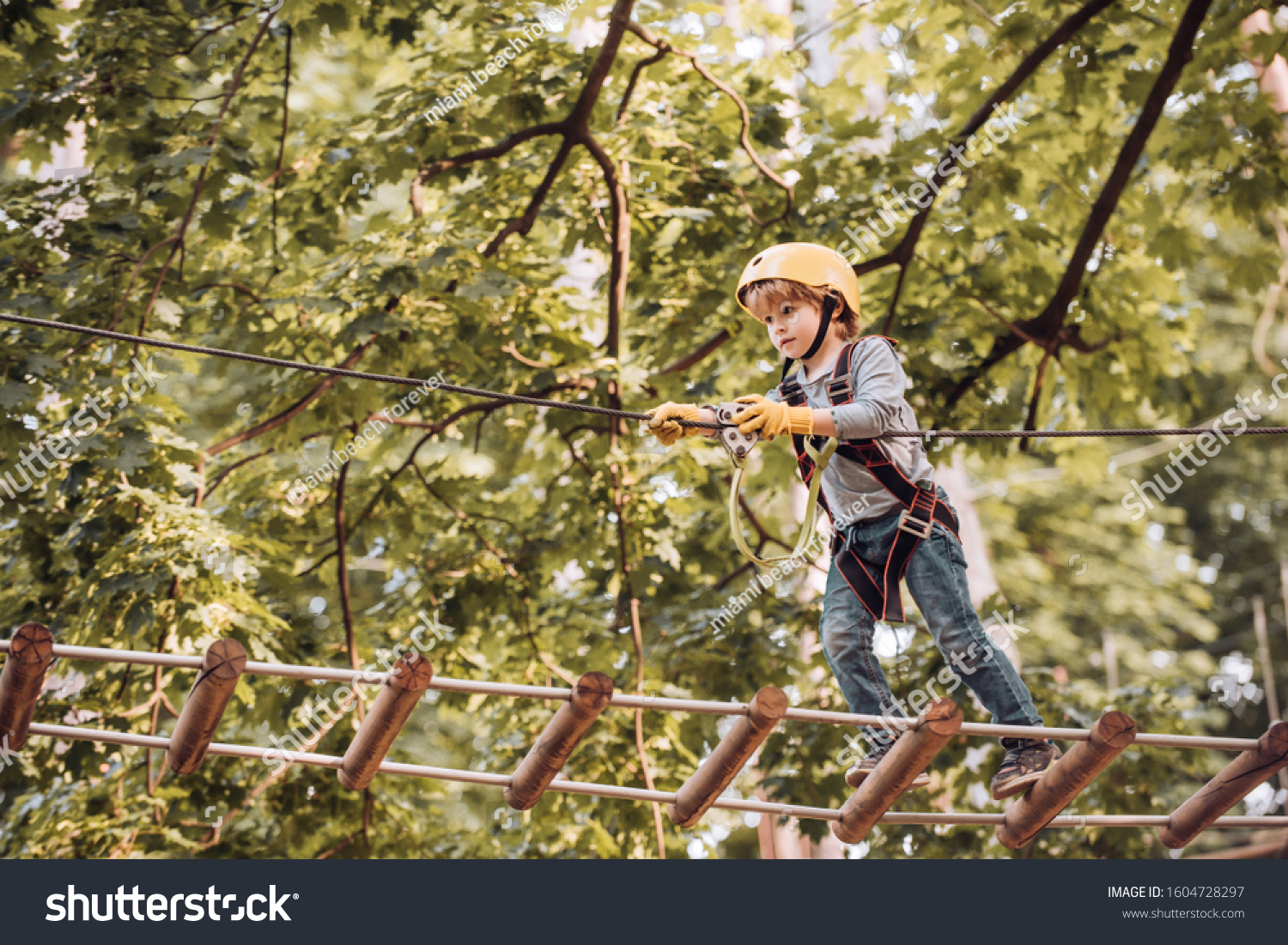 Balance beam and rope bridges. Go Ape Adventure. Child concept. Climber child on training. Portrait of a beautiful kid on a rope park among trees. Carefree childhood. #1604728297