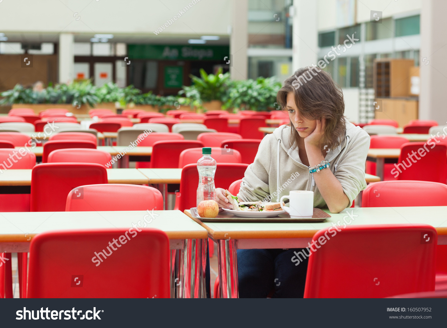 Alone and sad female student sitting in the cafeteria with food tray #160507952