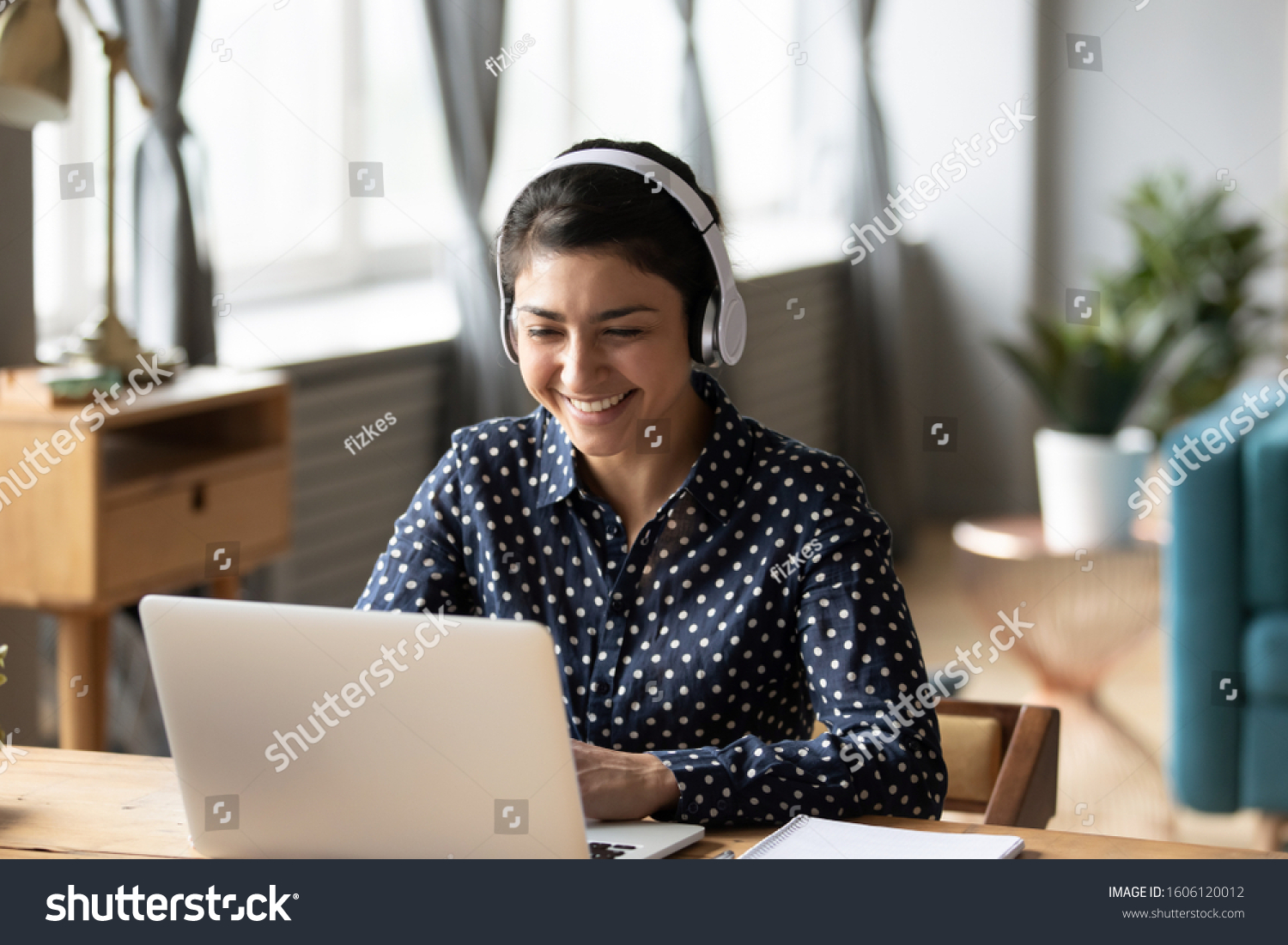 Happy indian young girl student wear headphone watch webinar listen online course communicate by conference video call e learn language in app laugh study with teacher lesson look at laptop at home #1606120012