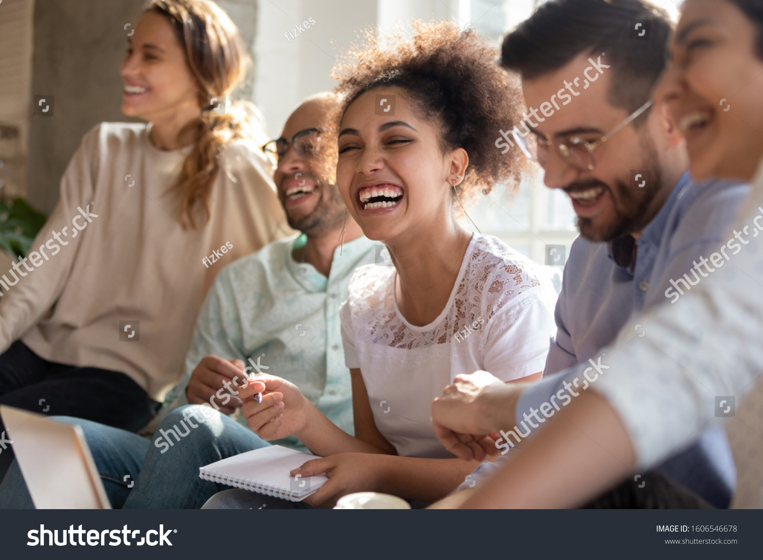 Overjoyed multiracial young people sit in row have fun laughing studying together indoors, happy international diverse students joke chat brainstorm preparing for test making notes learning #1606546678